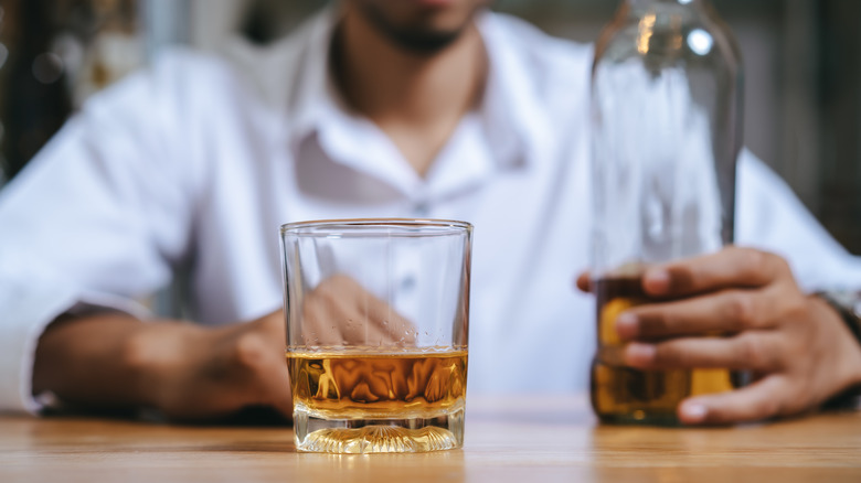 A man sits at a table with a glass of alcohol