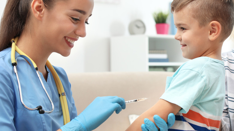 Smiling healthcare provider holding vaccine syringe up to young smiling boy