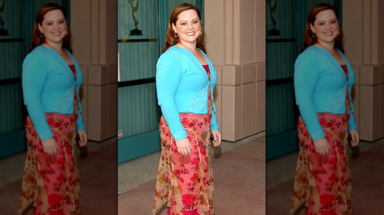 Melissa McCarthy smiling in a teal jacket and a dress