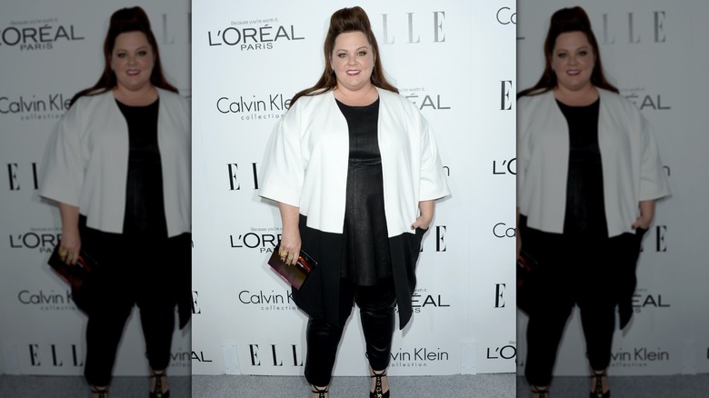 Melissa McCarthy smiling in a white jacket and a black top with jeans