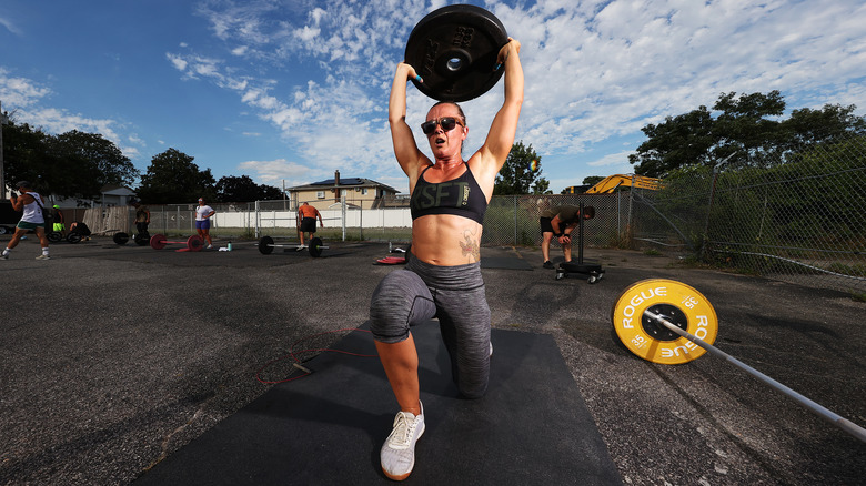 Woman doing a lunge while lifting a weight plate over her head