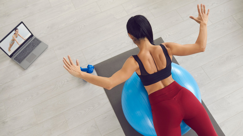 Woman on an exercise ball doing physical therapy exercises while looking at a laptop