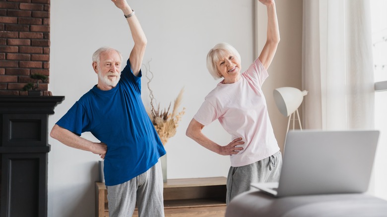 Older couple doing physical therapy exercises while looking at a laptop
