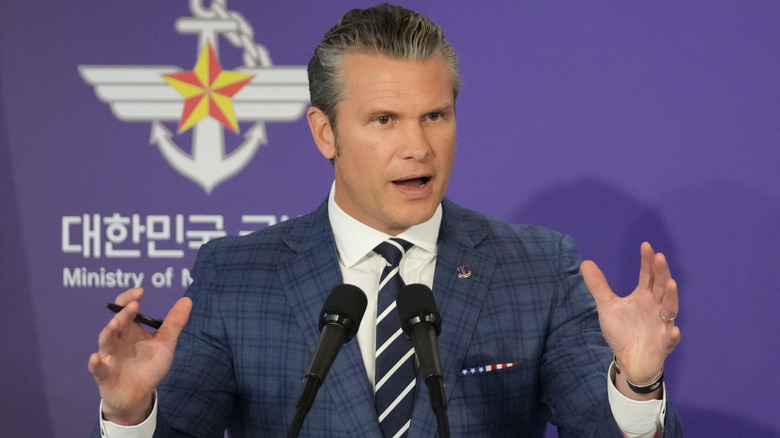 Pete Hegseth raising his hands at a conference
