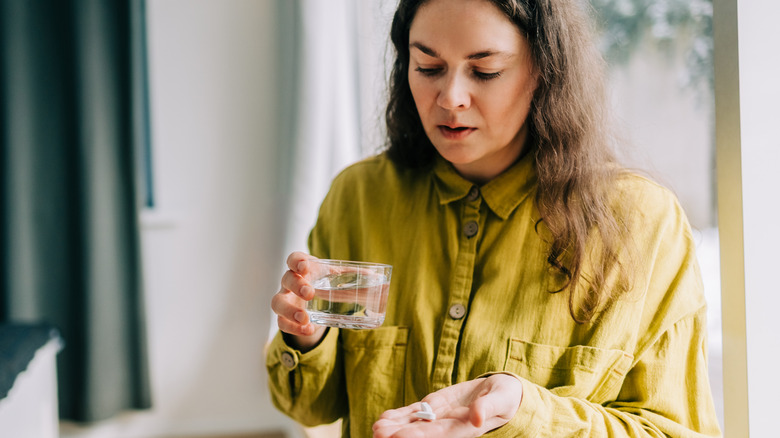 A woman holding medication in one hand and pills in another