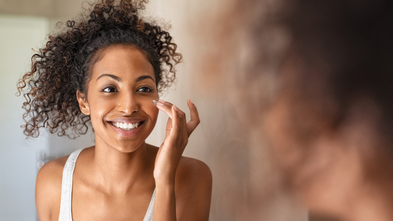 Woman smiling in mirror applying moisturizer