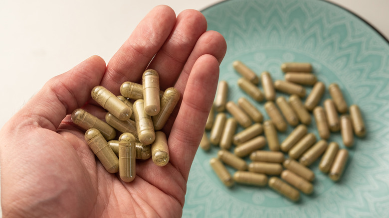 Hand holding kratom capsules