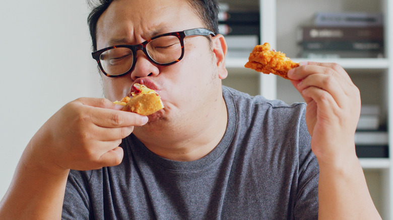 bespectacled man eating chicken and pizza