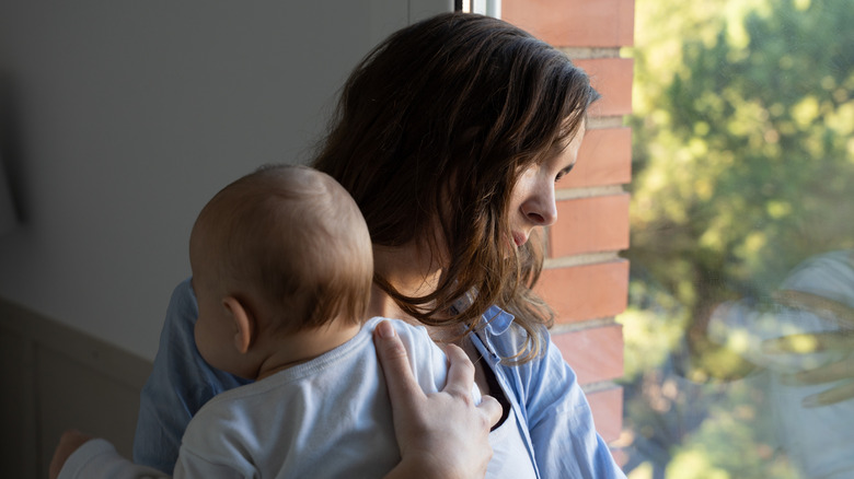 Postpartum mother looking out the window while holding her baby