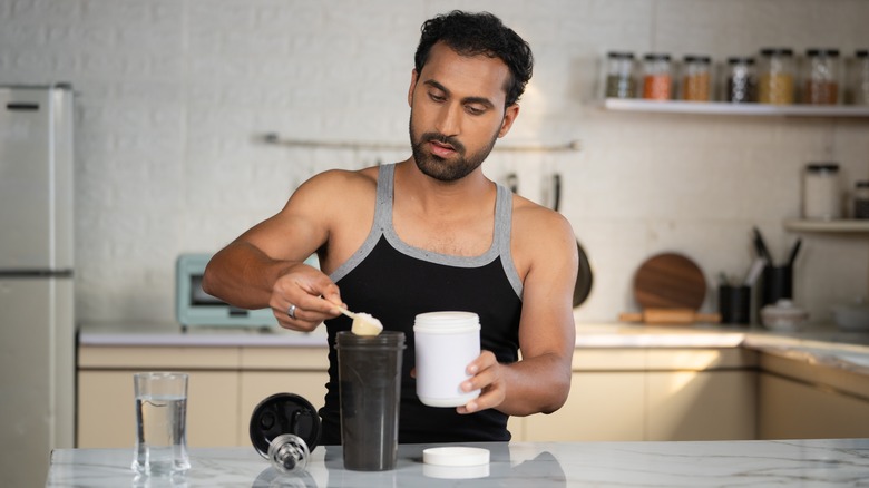 focused man scooping powder into smoothie