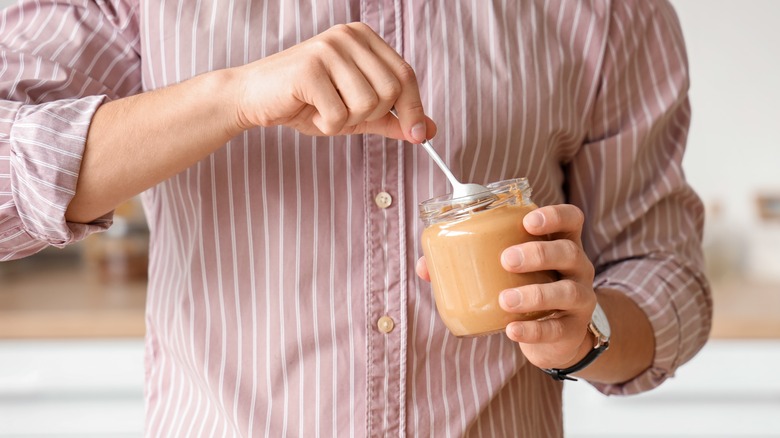 man's hand mixing peanut butter in glass jar in kitchen