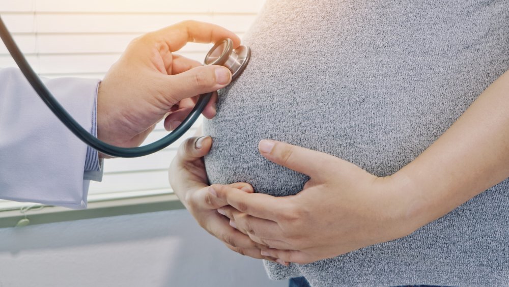 Doctor with stethoscope listens to a woman's pregnant belly