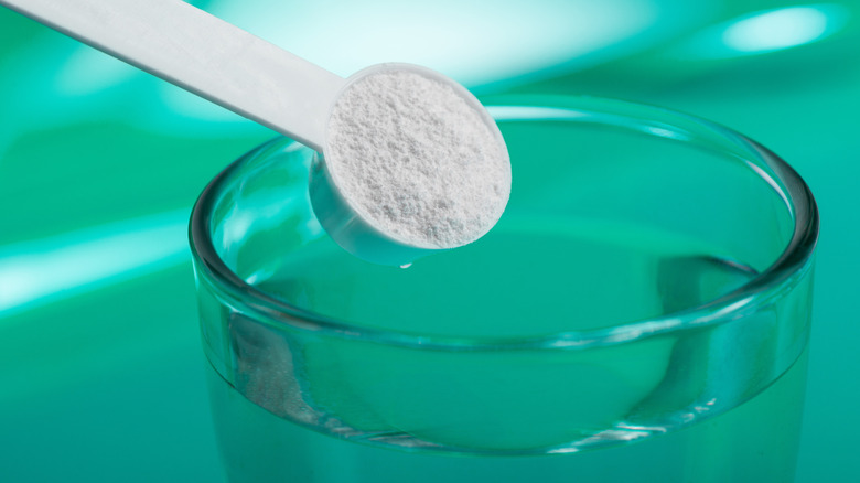 powdered supplement scoop over a glass of water