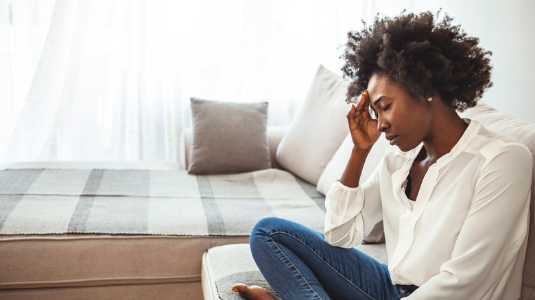 Black woman sitting on a couch with her head in her hand, looks upset