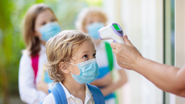 A child wears a mask and gets their temperature checked