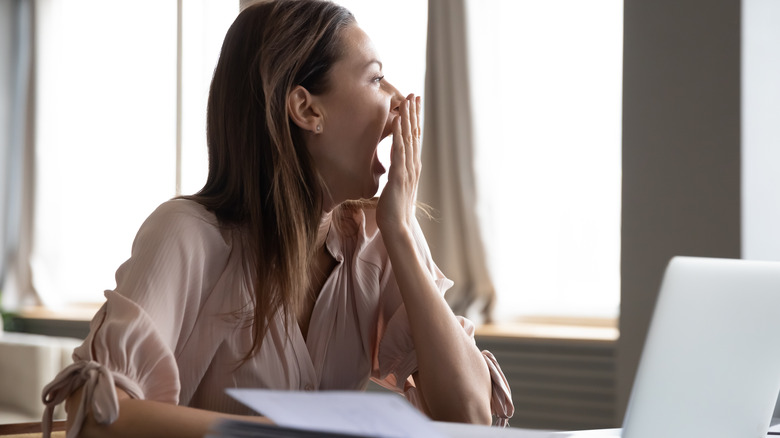 Woman yawning looking away from laptop