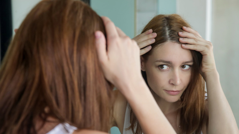 woman with red hair examining gray roots in mirror