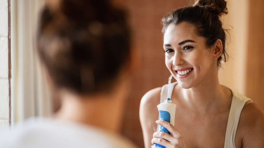 Woman smiling in mirror using a water flosser