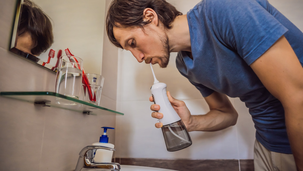 Man in bathroom using water flosser over sink