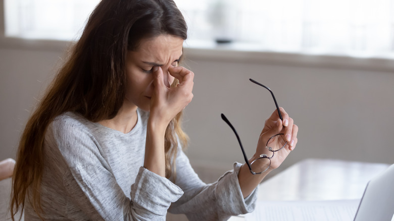 Woman pinching bridge of nose while holding eyeglasses