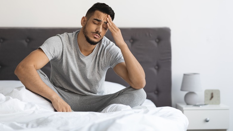 Man touching forehead in bed