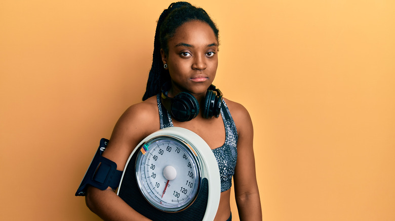 a beautiful woman looks at the camera while holding a scale in her arms 