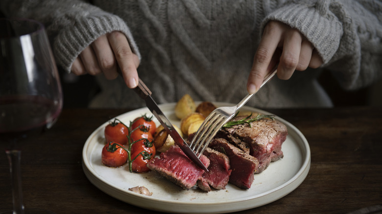 Hands cutting steak with utensils