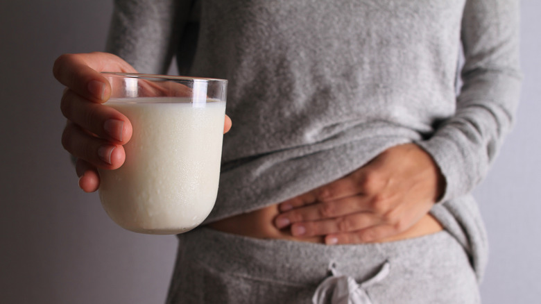 Woman holding a glass of milk and clutching her stomach