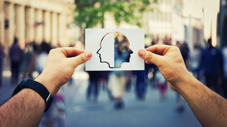 Man's hands holding a white paper sheet with two faced head over a crowded street background.