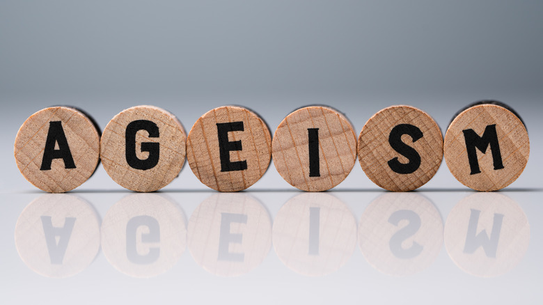 Ageism Text On Round Wooden Blocks Over Reflective White Desk