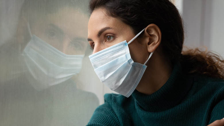 woman wearing a COVID mask while looking out the window