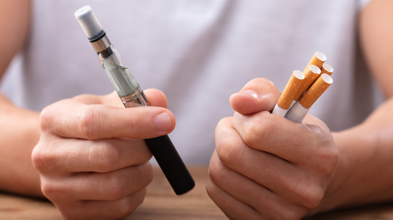 hands holding e-cigarette and tobacco cigarettes