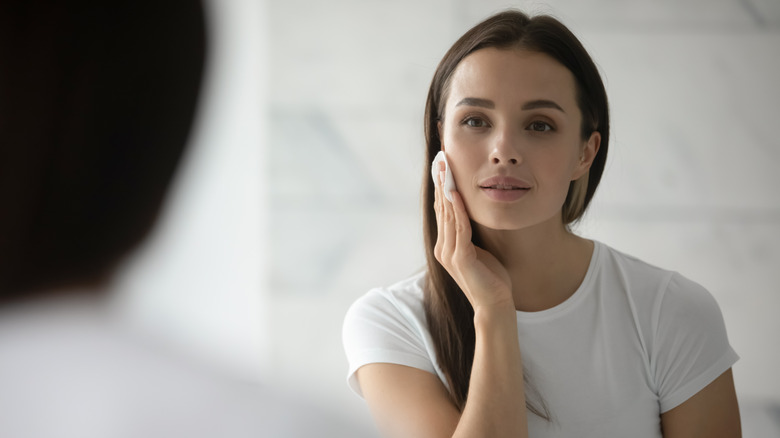 woman doing her skincare routine while looking in the mirror