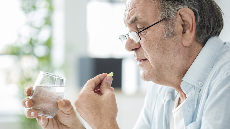 An elderly man taking a pill with water at home