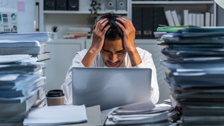 man frustrated in front of laptop with piles of documents