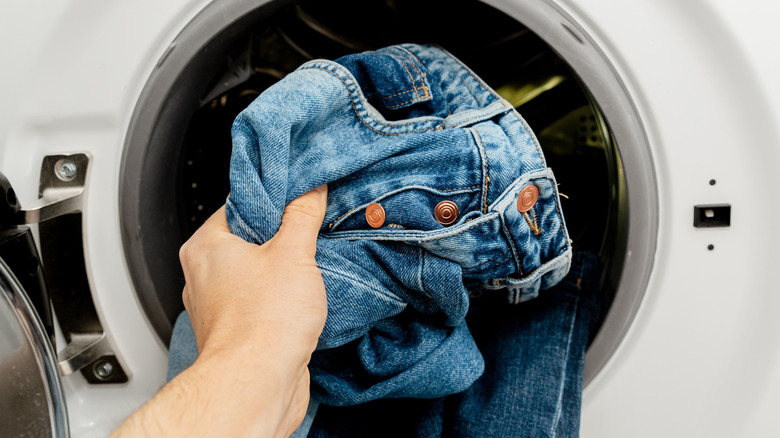 man putting pair of jeans into washing machine