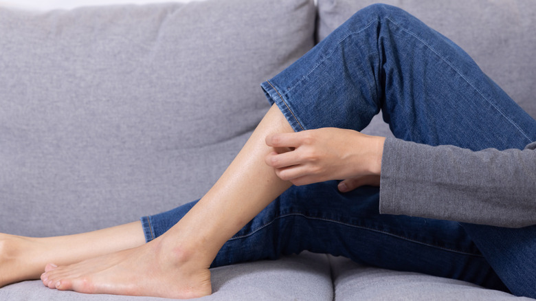 woman scratching her itchy leg while wearing jeans