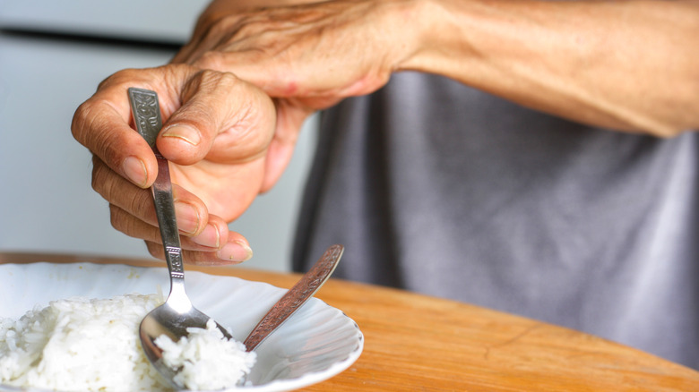 A man with Parkinson's holds his wrist while eating