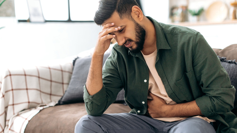 man sitting on sofa holding stomach in discomfort