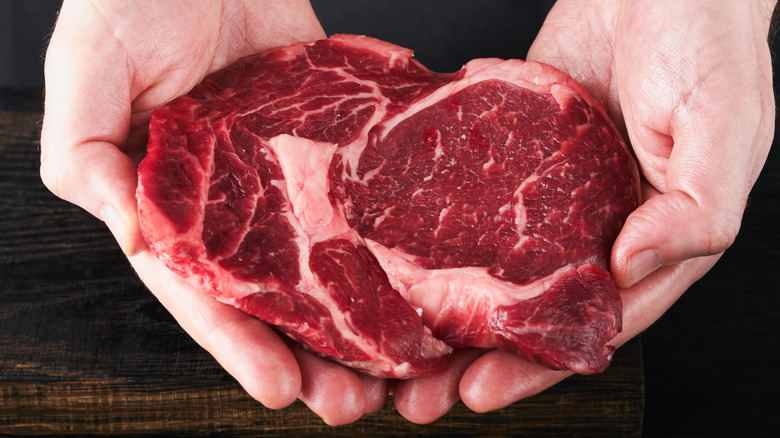 man holding raw ribeye cut of steak in hands