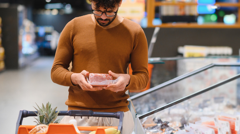 man looking at package of meat in store