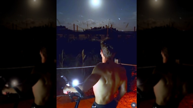 Ryan Seacrest from behind staring at the sky while shirtless with a bike