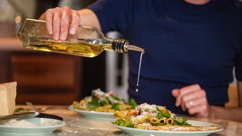 A man in pouring olive oil over his pasta.