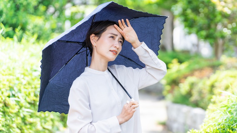 Overheated woman outside holding umbrella