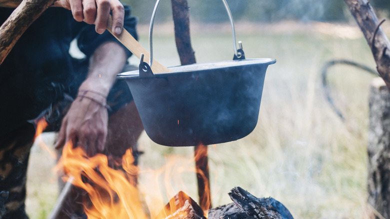 hand stirring a pot of stew over a fire outdoors