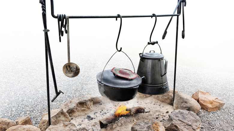A pot, ladle, and pitcher hang over a burning fire