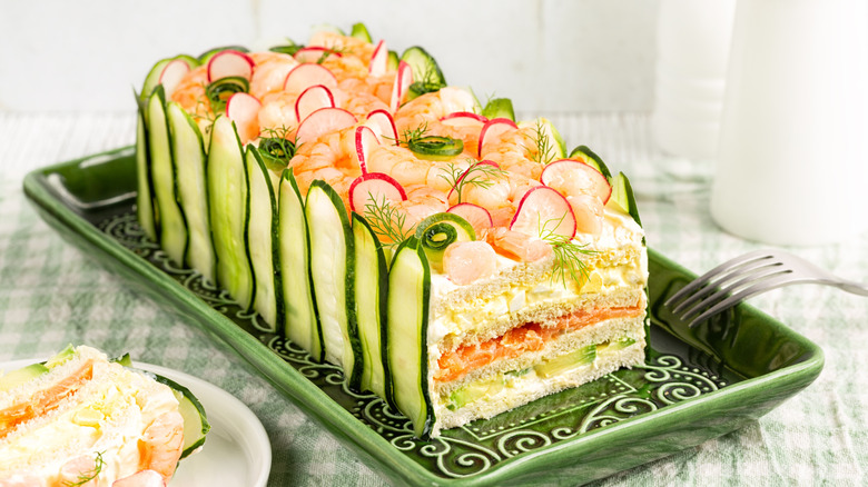 sandwich loaf cake made of layers of white bread with assorted salads and fillings between layers and covered in cream cheese and food decorations