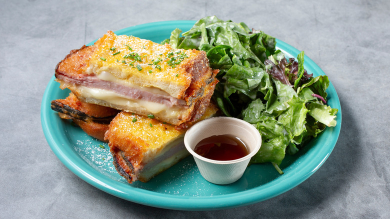 Monte Cristo sandwich dusted with powdered sugar served with a side of honey and green salad