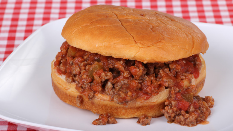 Sloppy Joes sandwich in a burger bun on a white plate over picnic table