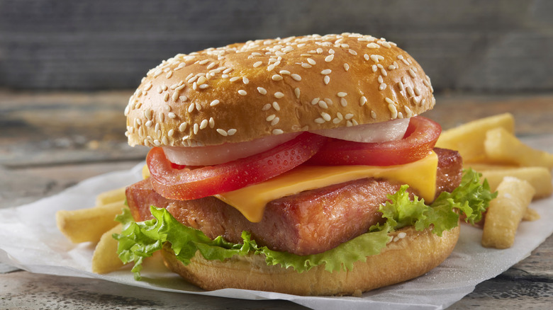 Spam sandwich in burger bun with lettuce, tomato, onions, cheese, and a side of fries
